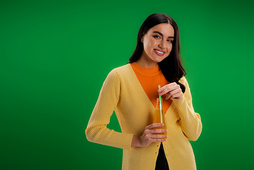 young brunette woman with bottle of natural juice smiling at camera isolated on green