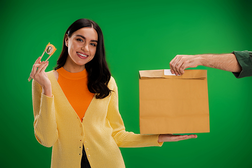 happy woman holding sushi roll with chopsticks near man with paper bag isolated on green