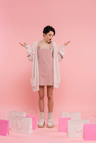 full length of amazed woman showing wow gesture while looking at shopping bags on pink background