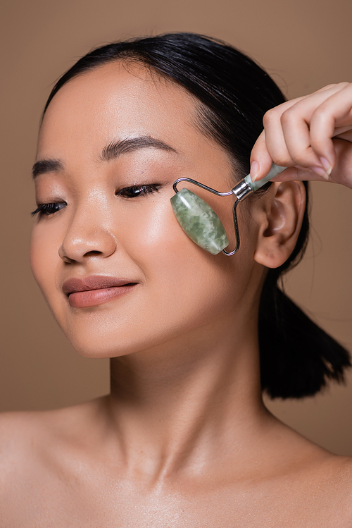 Pretty asian model using jade roller on face isolated on brown