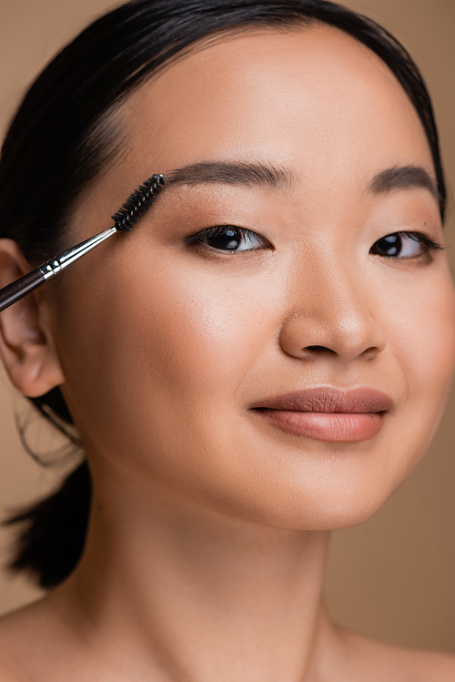 Portrait of young asian woman with makeup holding eyebrow brush isolated on brown