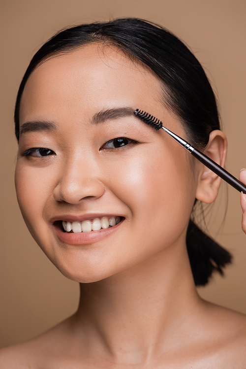 Pretty asian model styling eyebrow while holding brush isolated on brown