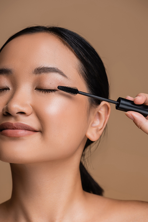 Cropped view of young asian woman holding applicator for mascara isolated on brown