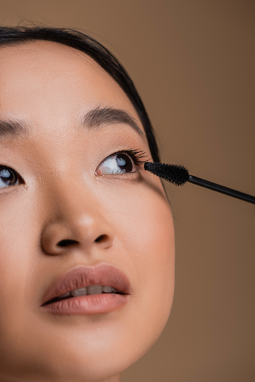 Cropped view of asian woman with makeup holding mascara applicator isolated on brown