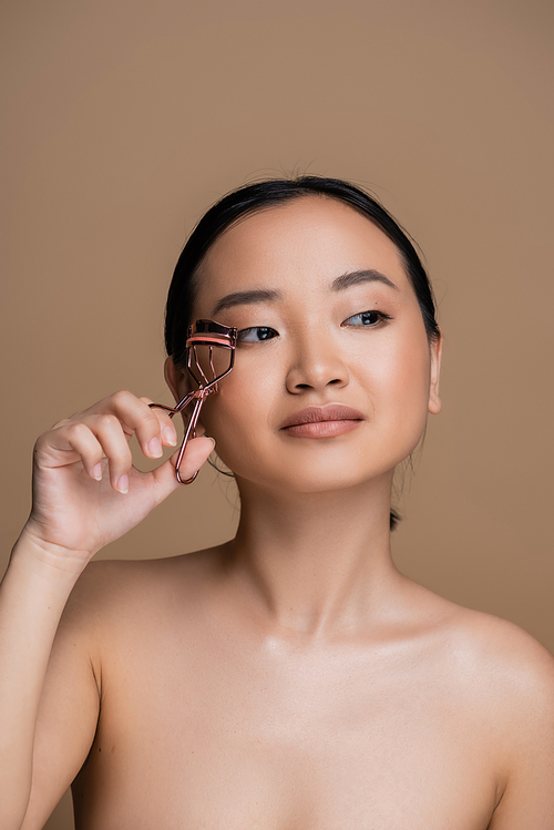 Young asian woman with naked shoulders holding lush curler isolated on brown