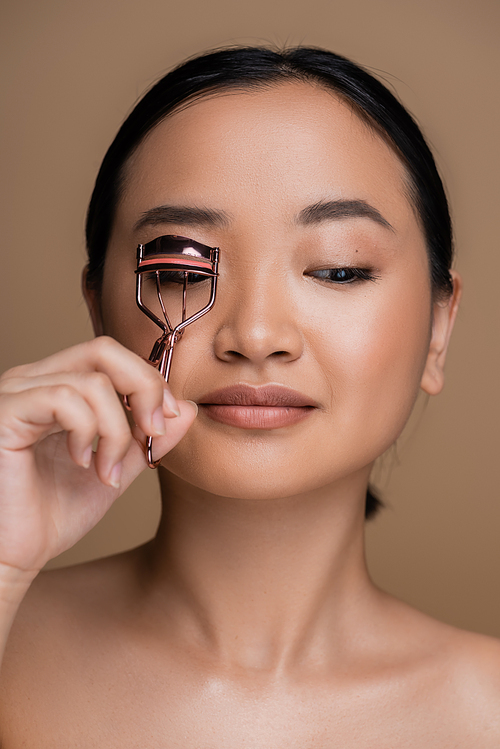 Asian model with makeup using lush curler isolated on brown