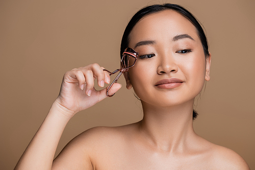 Pretty asian woman holding lush curler near face isolated on brown