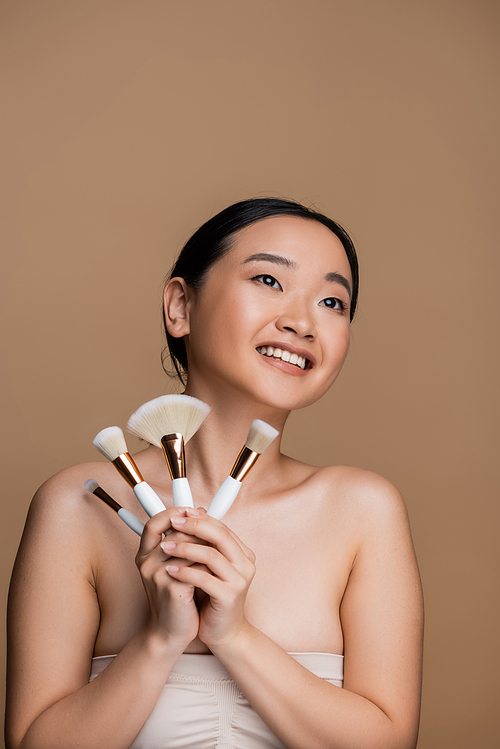 Positive asian model in top holding cosmetic brushes isolated on brown