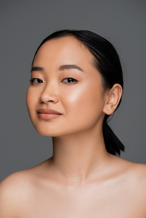 Young asian woman with naked shoulders looking at camera isolated on grey