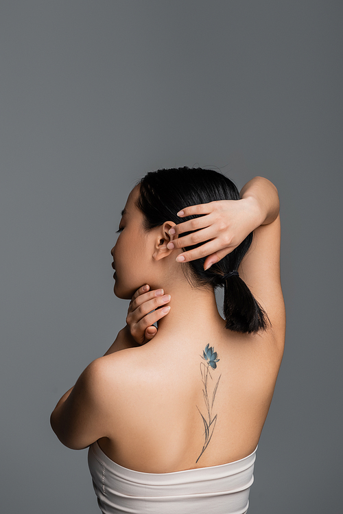 Side view of tattooed asian woman touching hair isolated on grey