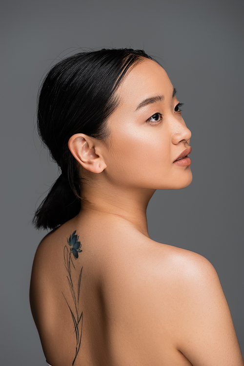 Brunette asian woman with tattoo on back looking away isolated on grey
