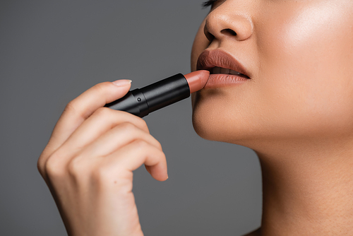 Cropped view of young woman applying lipstick isolated on grey