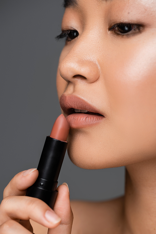 Cropped view of asian woman applying beige lipstick isolated on grey