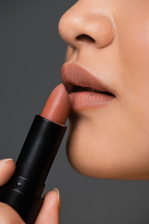 Close up view of woman applying beige lipstick isolated on grey