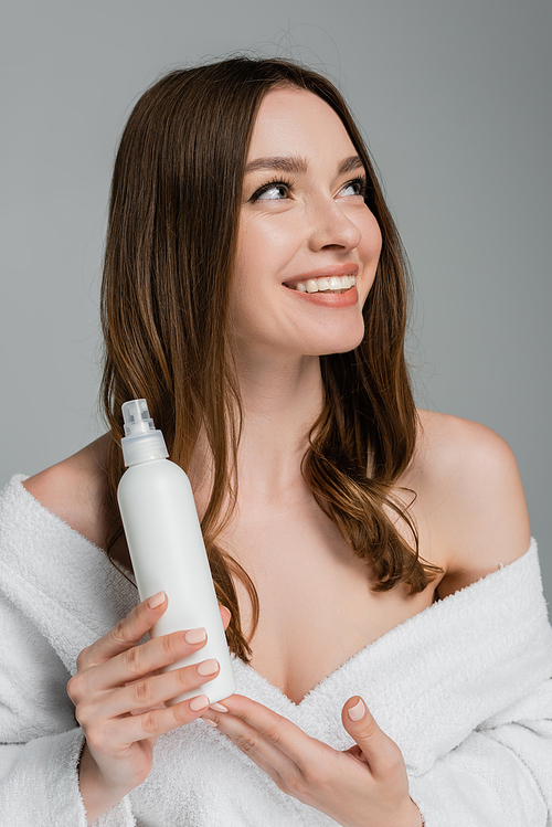 smiling young woman with shiny hair holding hair spray isolated on grey
