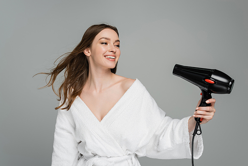 happy young woman with shiny hair using hair dryer isolated on grey
