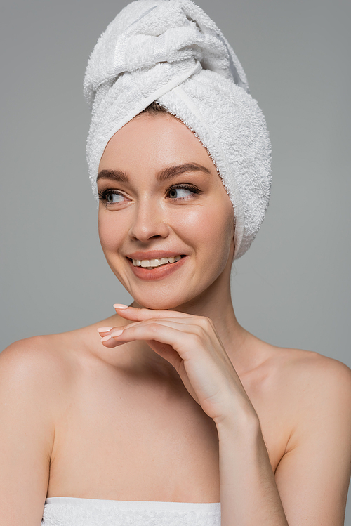 cheerful young woman with bare shoulders and towel on head isolated on grey