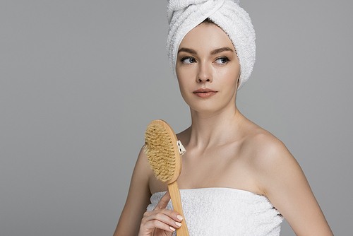 young woman with towel on head holding wooden hair brush isolated on grey