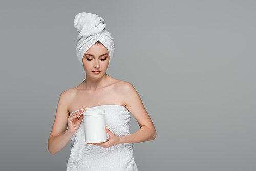 young woman with towel on head holding container with hair mask isolated on grey