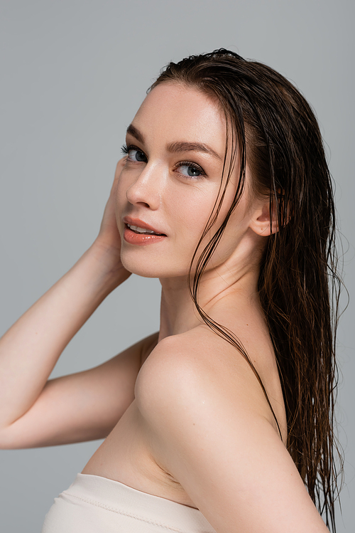 smiling young woman with wet hair and bare shoulders looking at camera isolated on grey
