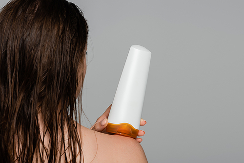 back view of young woman with wet hair holding bottle with shampoo isolated on grey