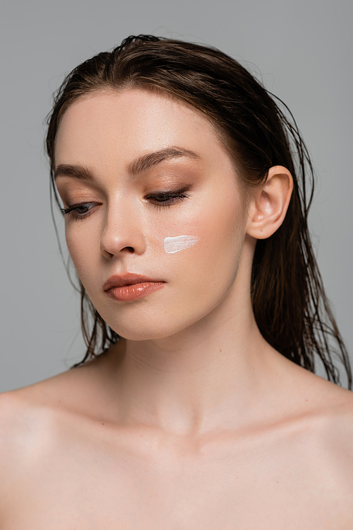 portrait of pretty young woman with wet hair and moisturizing cream on cheek isolated on grey