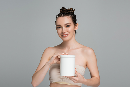 cheerful young woman with wet hair holding container with mask isolated on grey