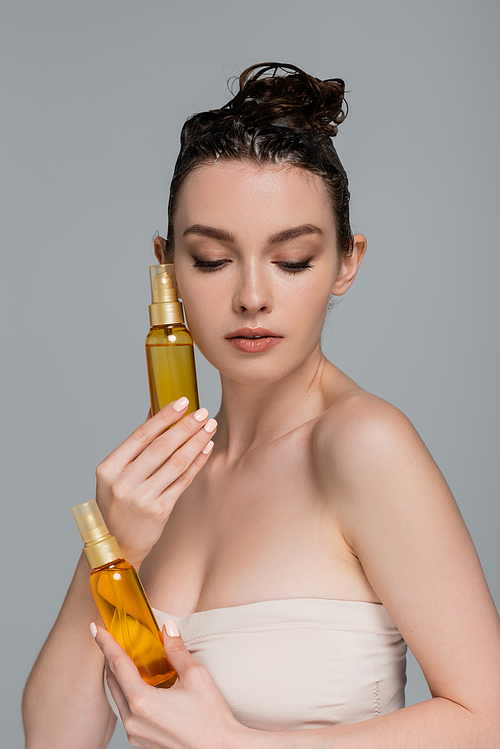 pretty young woman with wet foamy hair holding bottles with treatment oil isolated on grey