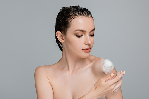 young woman with wet hair touching bare shoulder with white foam isolated on grey