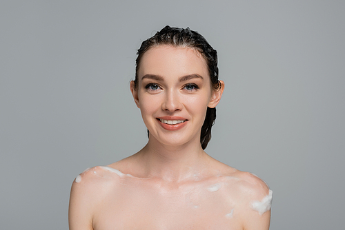 happy young woman with wet hair and bare shoulders smiling isolated on grey
