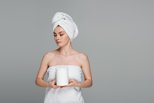 young woman with white towel on head holding jar with hair mask isolated on grey
