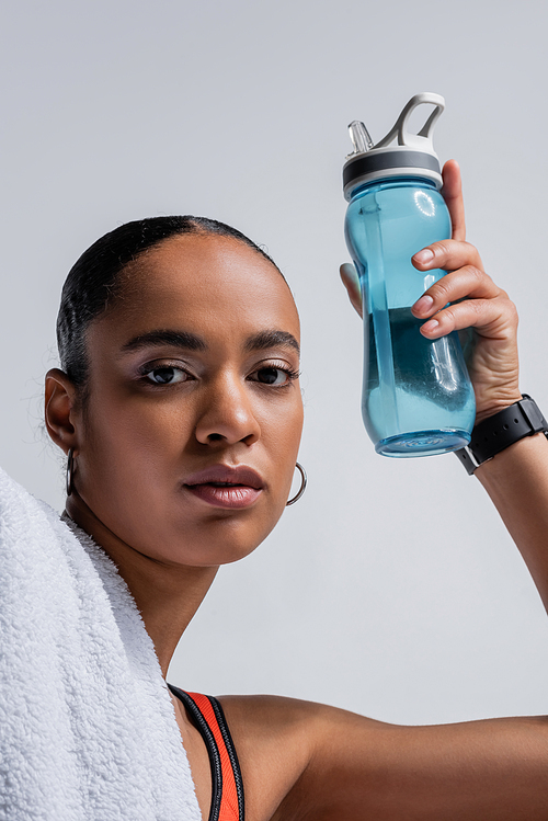 brunette african american woman in sports bra holding sports bottle with water isolated on grey