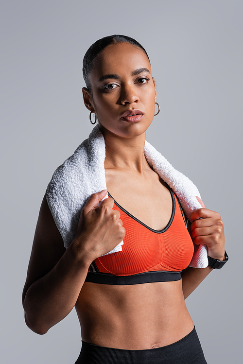 young african american sportswoman in red sports bra standing with towel isolated on grey