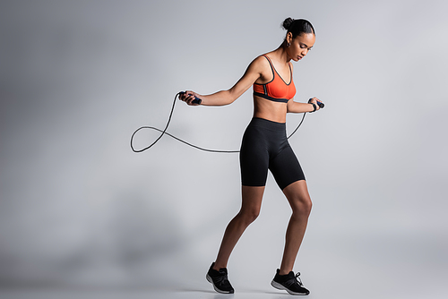 full length of sportive african american woman exercising with skipping rope on grey