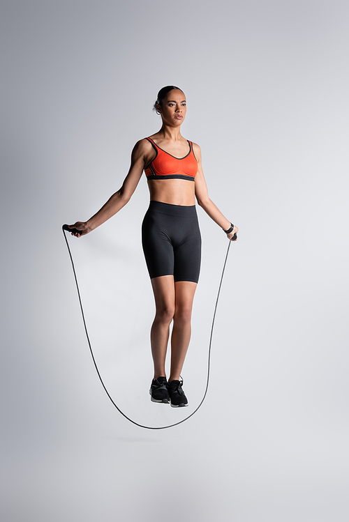 full length of african american sportswoman exercising with skipping rope on grey