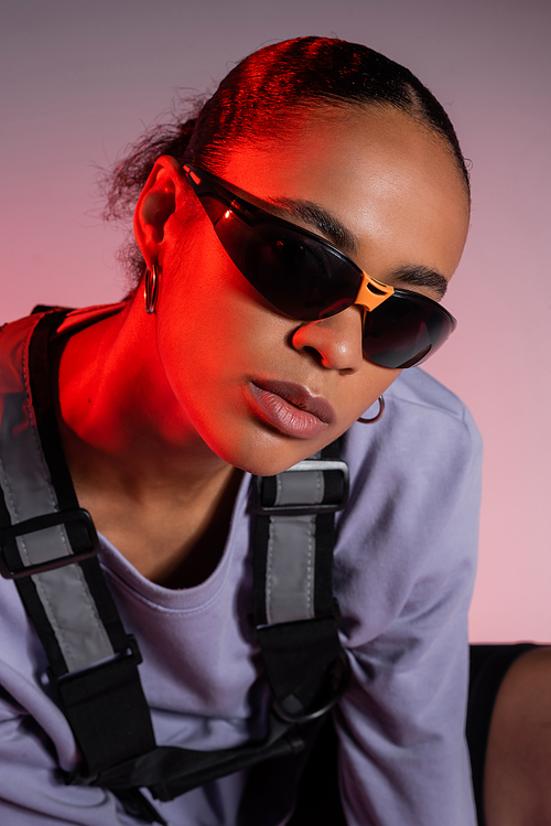 african american woman in sweatshirt and stylish sunglasses on grey with red light