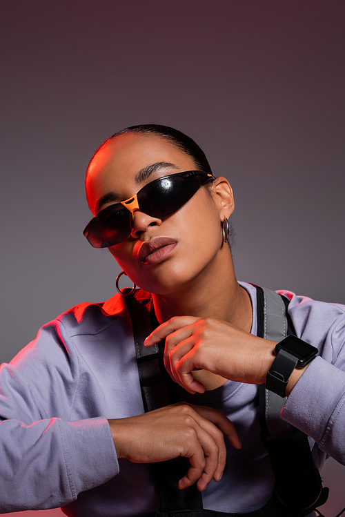 portrait of african american woman in trendy sunglasses looking at camera on grey with red light