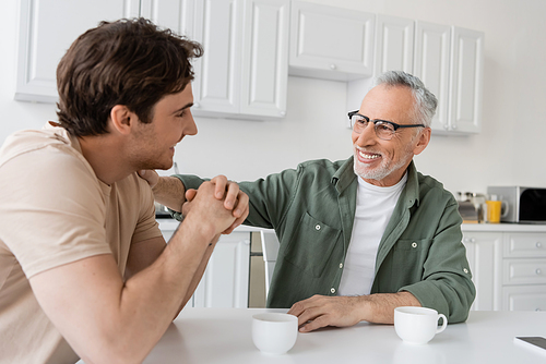 cheerful and mature father in eyeglasses hugging shoulder of happy son during breakfast