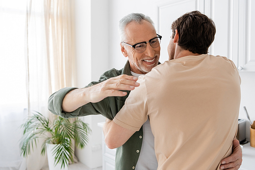 happy mature man in eyeglasses embracing young son at home