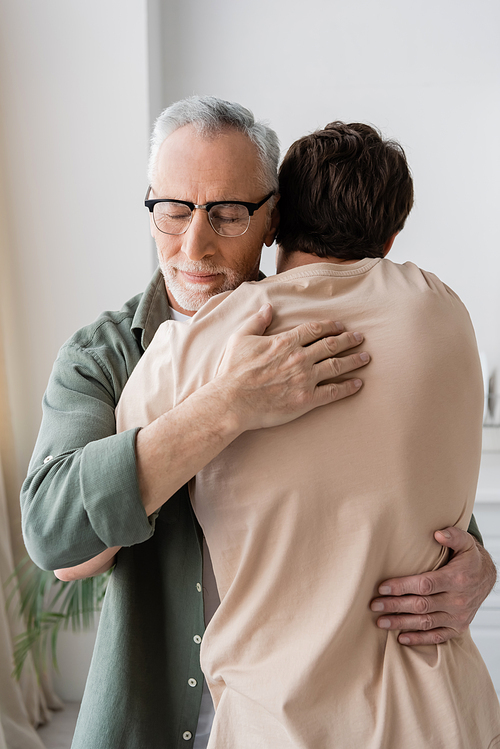 senior man with closed eyes hugging adult son at home