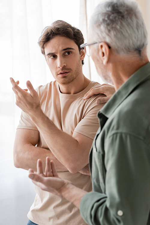 mature man touching shoulder and talking to upset son on blurred foreground