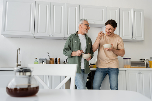 mature man smiling while talking to young cheerful son during breakfast in kitchen