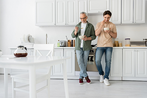 full length of mature father and young son having breakfast while standing in modern kitchen