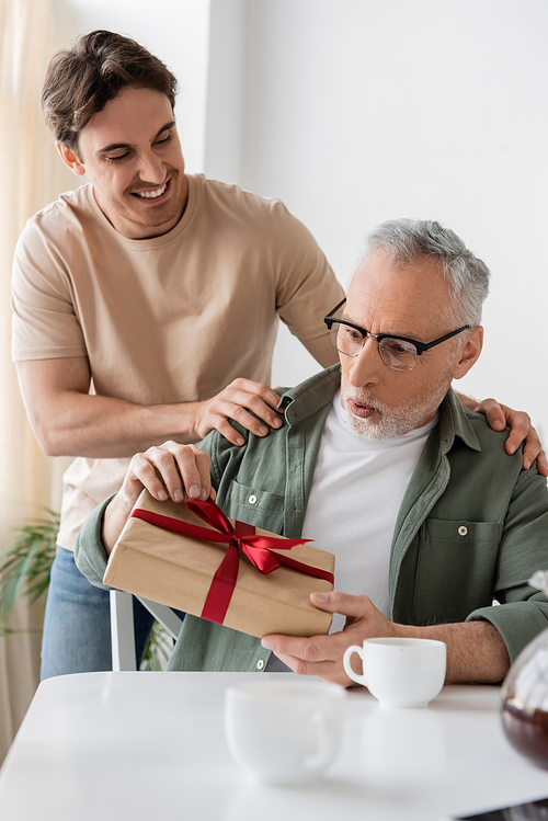 amazed man in eyeglasses holding fathers day present near smiling son