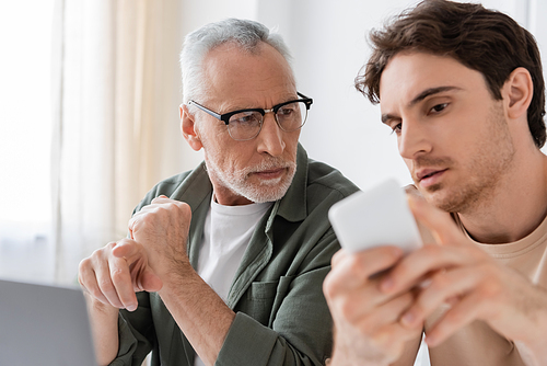 young man showing blurred smartphone to senior dad in eyeglasses