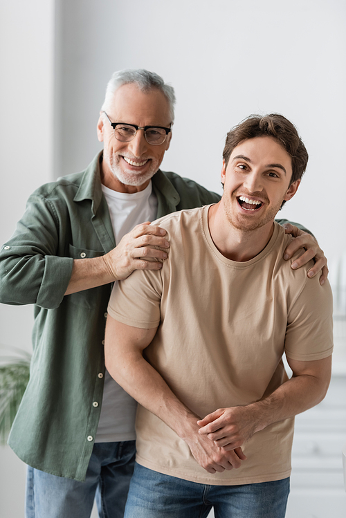 smiling man in eyeglasses hugging shoulders of excited son while looking at camera