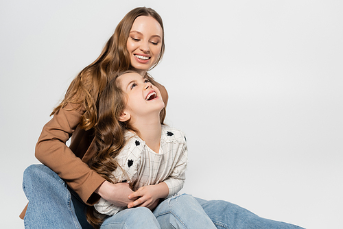 happy woman embracing laughing daughter isolated on grey