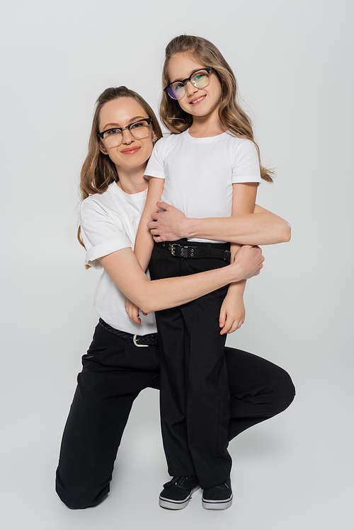mom and daughter in eyeglasses and black and white clothes looking at camera on grey background