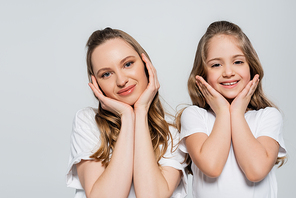 pleased mother and child with hands near face looking at camera isolated on grey