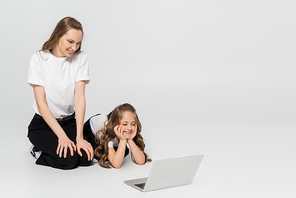 cheerful mother and daughter watching movie on laptop on grey background